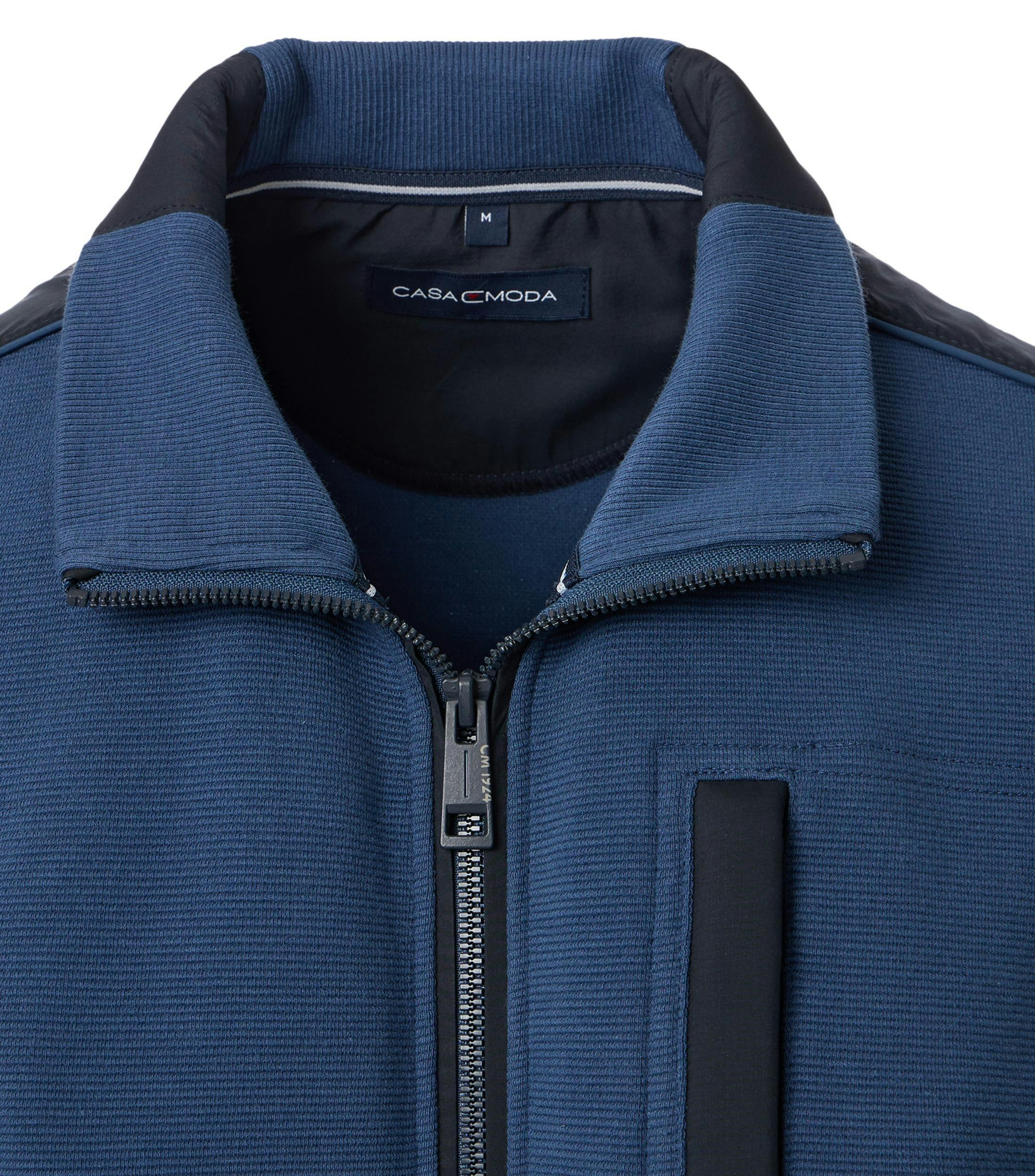 Das Model trägt eine Sweatjacke im uni Muster in der Farbe mittleres Dunkelblau