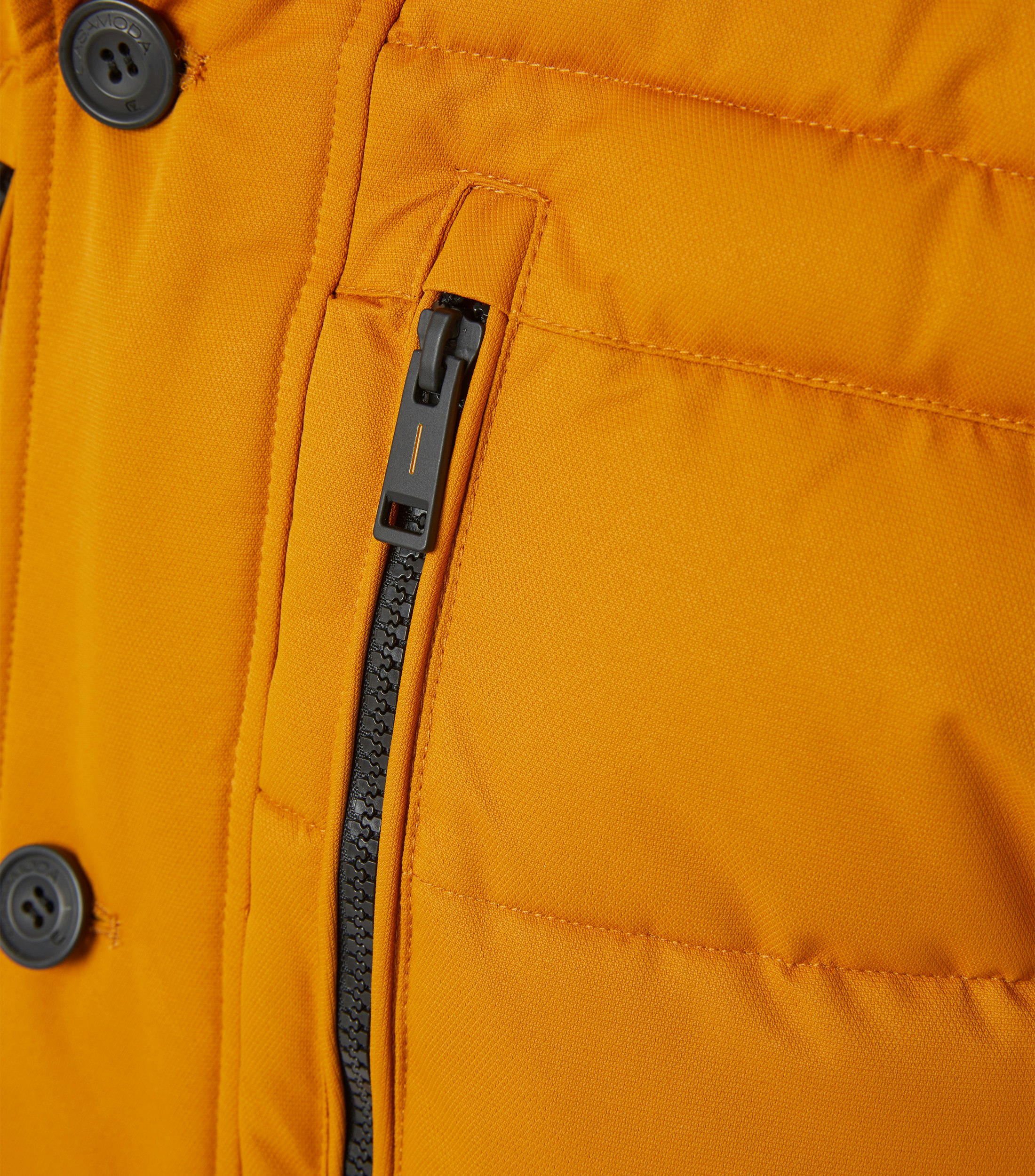 Das Model trägt eine Jacke im uni Muster in der Farbe Honiggelb