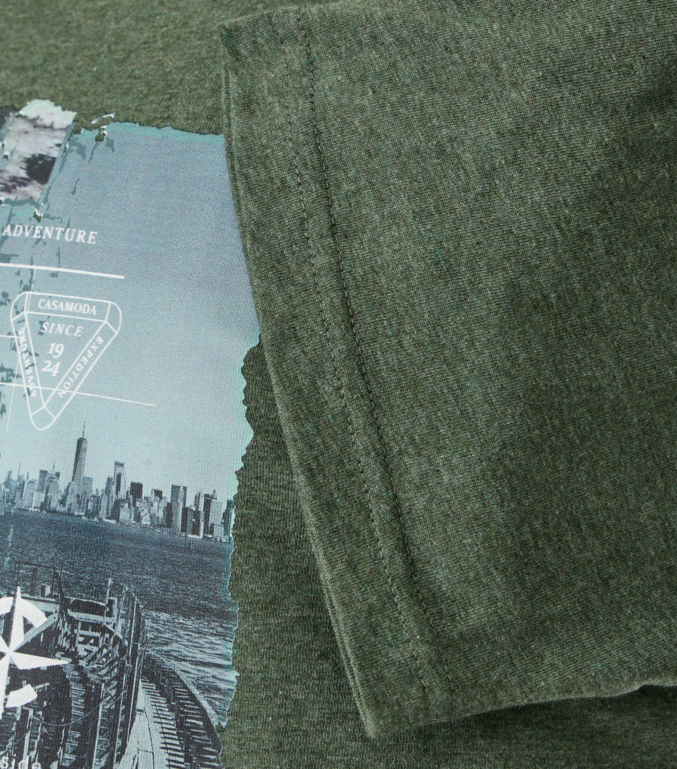 Das Model trägt ein TShirt im uni Muster in der Farbe Grün