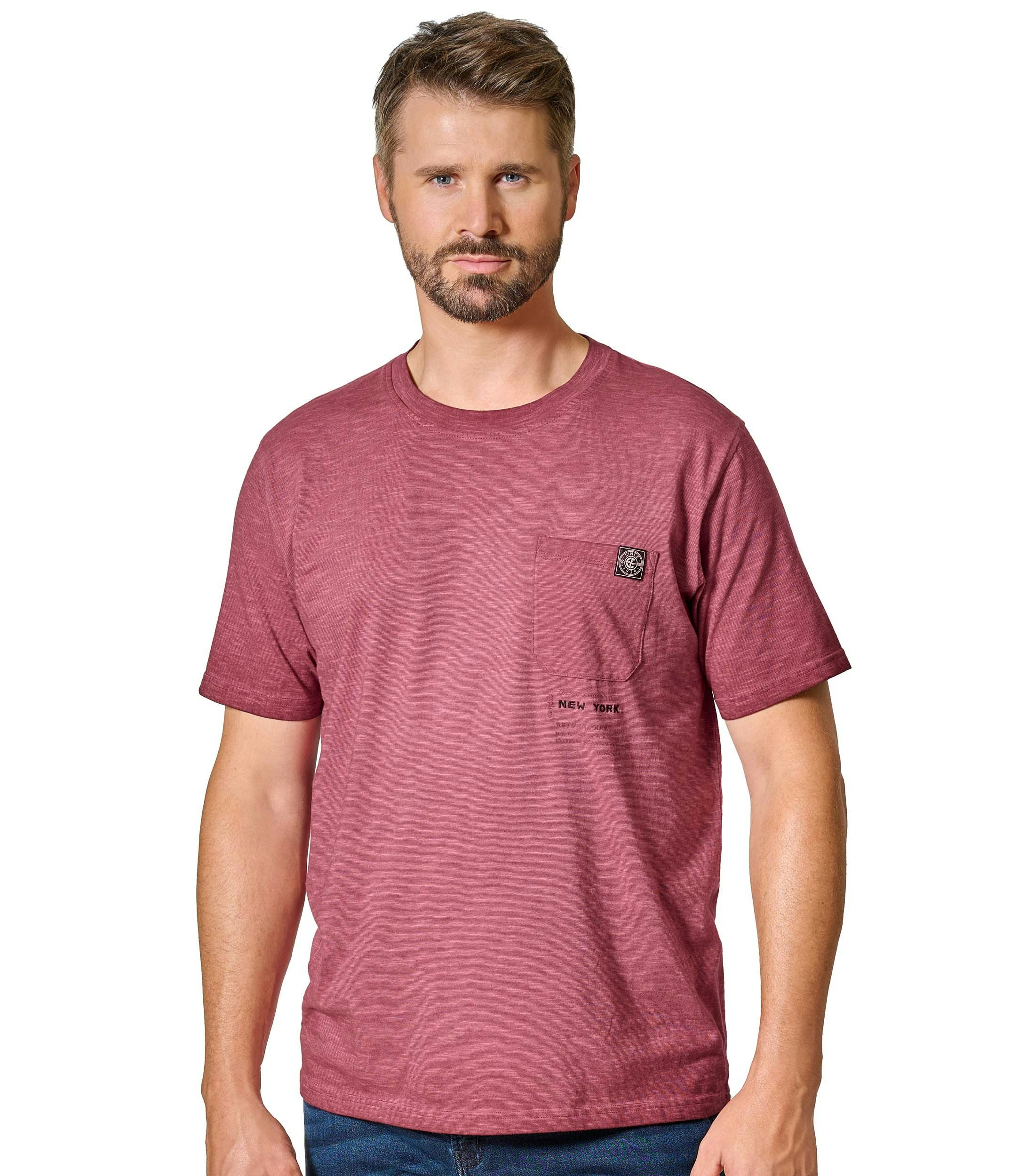 Das Model trägt ein TShirt im uni Muster in der Farbe Rotorange